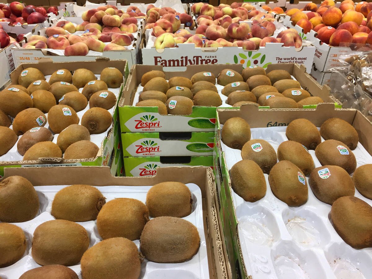 A variety of fruit, including kiwi fruit and peaches, sits in cases on display in a grocery story.