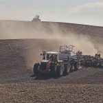 A tractor pulls an air seeder down a hill while a grain truck is parked at the top.