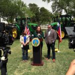 U.S. secretary of agriculture Brooke Rollins speaks to farmers and media from a podium in a yard with tractors parked behind her.