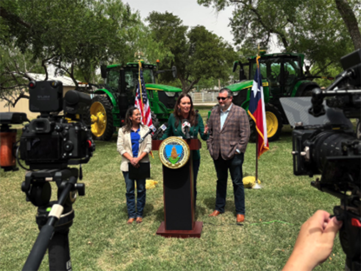 U.S. secretary of agriculture Brooke Rollins speaks to farmers and media from a podium in a yard with tractors parked behind her.