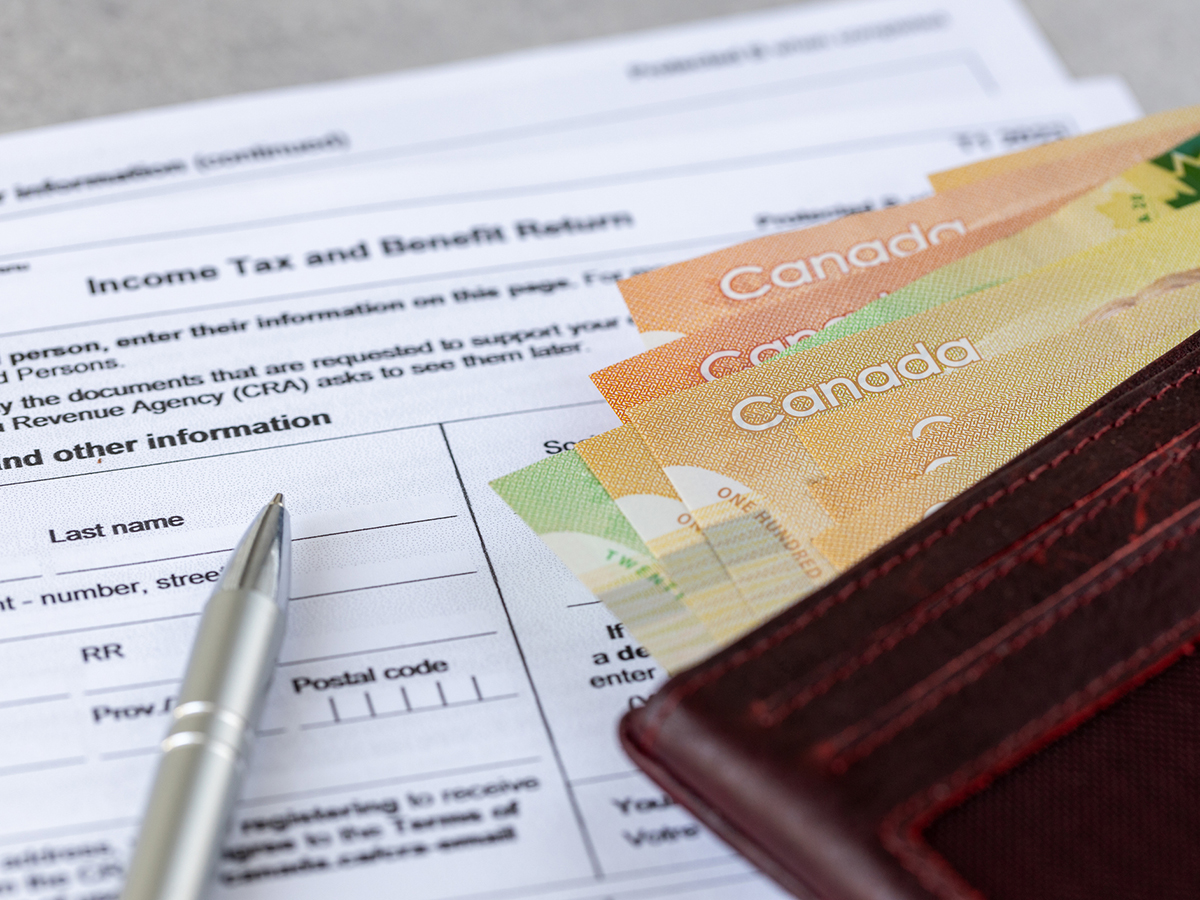 A close-up of a tax/benefits form with a pen sitting on it as well as a wallet that has a number of large denomination bills - based on their colour - sticking out of it.