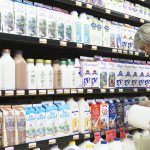 A woman looks at a jug of milk in front of a dairy display cooler in a grocery store.