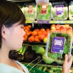 A woman looks at a package of "organic mixed baby greens" in a grocery store's produce section.