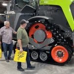 Two men stand beside the massive tracks on a new Claas Xerion tractor at Canada's Farm Show in Regina.
