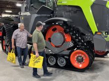Two men stand beside the massive tracks on a new Claas Xerion tractor at Canada's Farm Show in Regina.