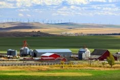 A scenic farm yard in Alberta sits at the base of some hills that are dotted with wind turbines in the distance.