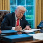Donald Trump sits at his desk in the Oval Office signing executive orders.