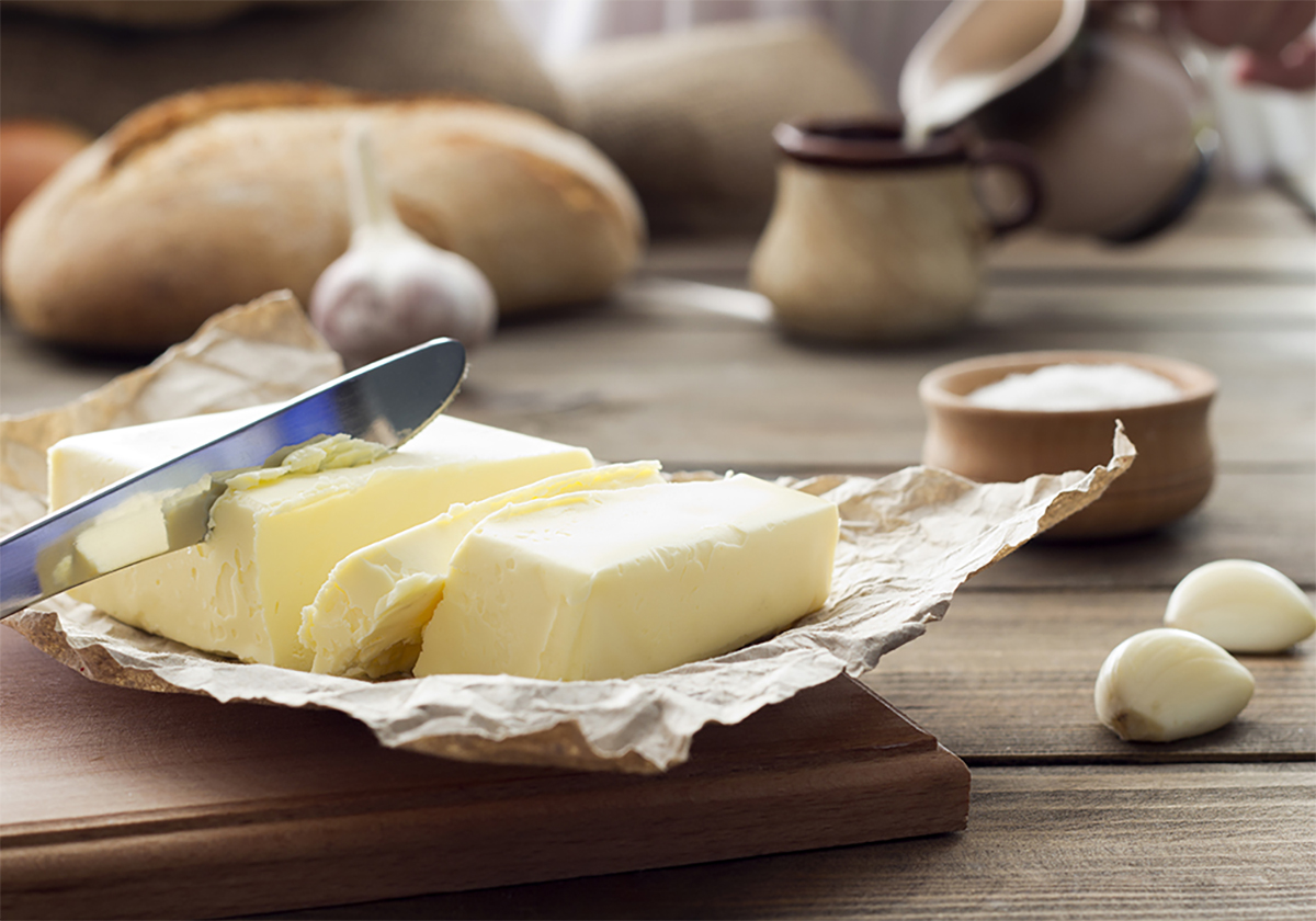A block of butter is cut into sticks and sits on its foil wrapper on a cutting board on a wooden table.