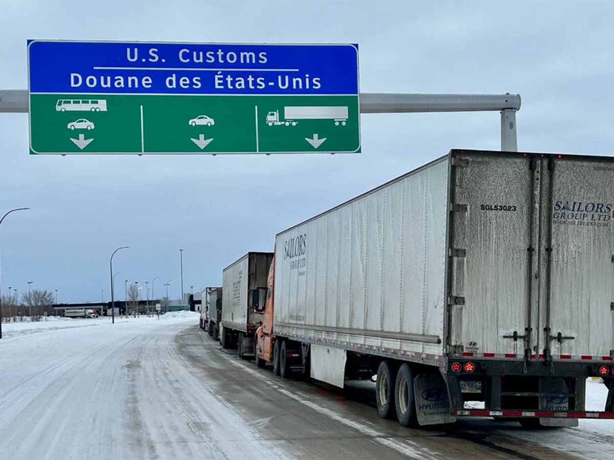 Trucks are lined up on a highway under as sign that reads, "U.S. Customs" as they wait to cross the border.