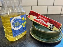 A stick of butter and a container of canola oil sit next to one another on a kitchen counter.