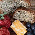 Cheese, strawberries, blueberries and banana bread all sit on a wooden table.