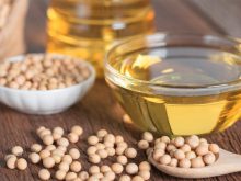 Soybeans sit in a bowl and some are spilled on a table top next to a bowl of seed oil.