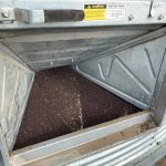 Canola seed is visible when the access door is removed from a steel grain bin.