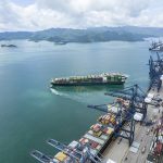 A large, fully-loaded container ship leaves the dock at a busy container port in China.