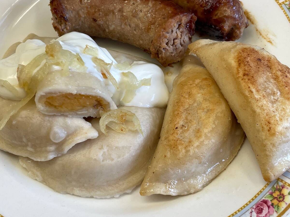 Potato and cheddar cheese pierogies with sour cream and sautéed onions on a plate with some sausage in the background.