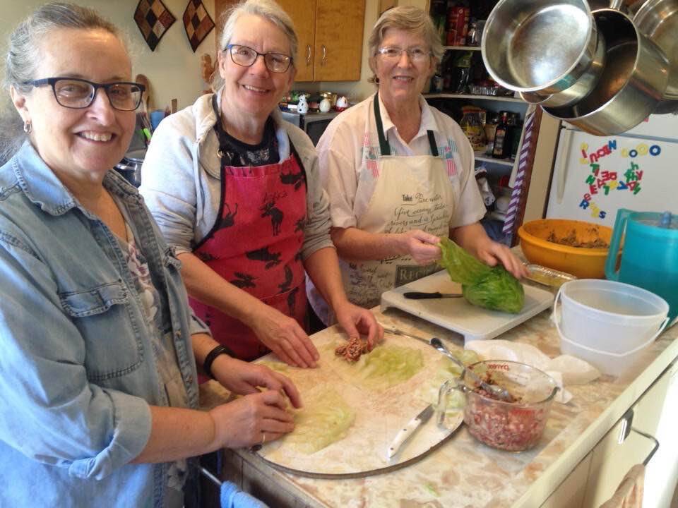 Three women have teamed up and are making cabbage rolls on an assembly line in a kitchen.