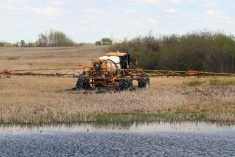 A high clearance sprayer works near a slough.
