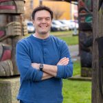 Promotional photo of B.C. NDP member of parliament Alistair MacGregor standing among some totem poles.