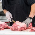 A butcher cuts meat on a counter.
