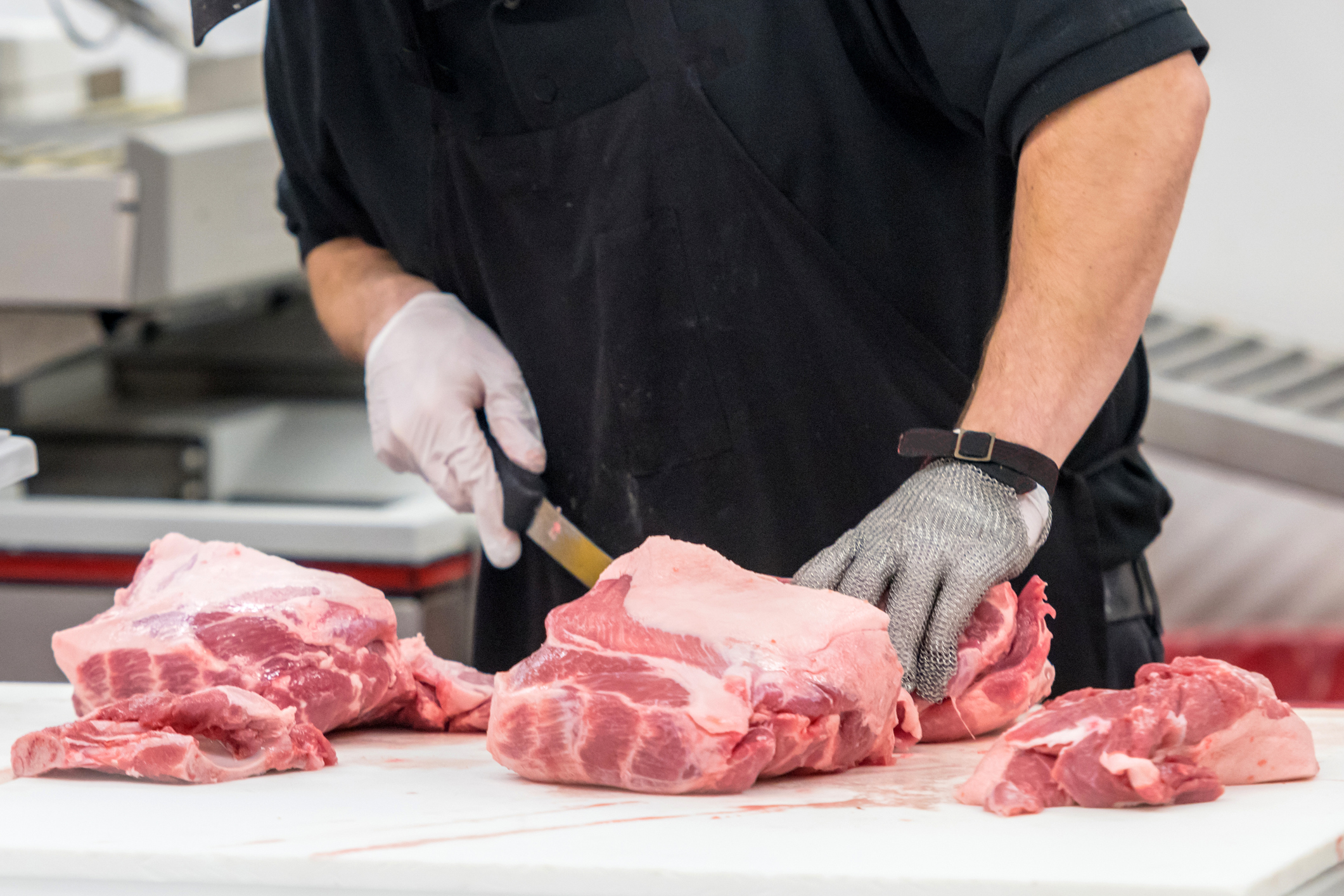 A butcher cuts meat on a counter.