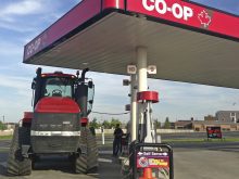 A large red tractor with tracks fills up with fuel at a Co-Op gas station.