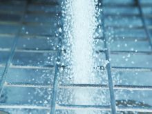 Close-up of white fertilizer granules pouring through a metal screen.
