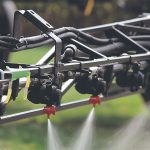 Liquid flows from the nozzles on a high clearance sprayer's boom.