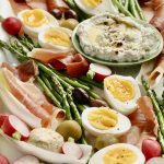Hard boiled eggs cut in half, veggies and meat on a tray.