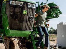A female farmer climbs down from a sprayer.