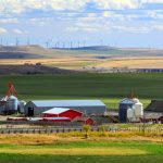 A scenic farm in the Alberta foothills with wind turbines on a ridge in the distance.