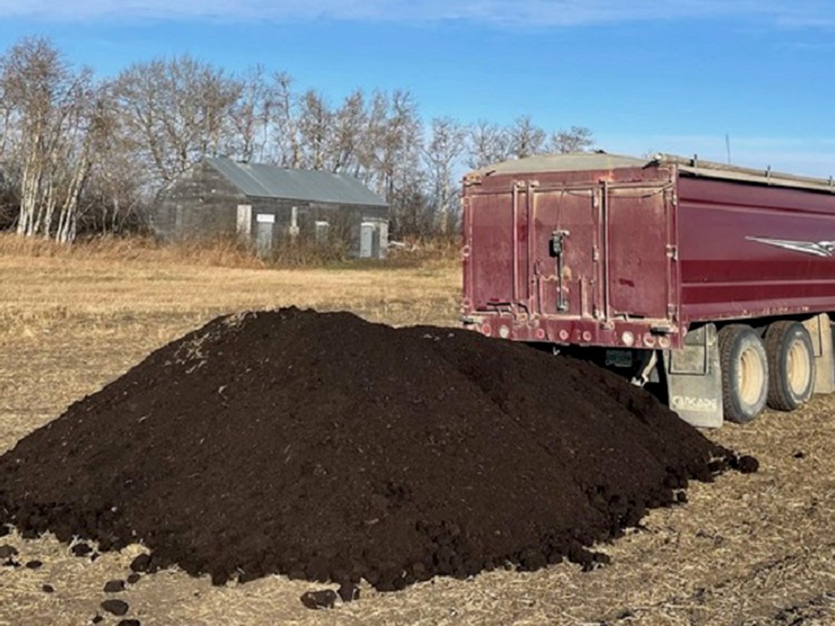 A pile of dark compost sits on the ground behind a tandem axle dump truck.