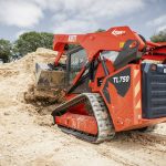A red Kioti track loader is dumping a bucketload of sand.