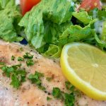 Oven roasted salmon teamed with herbs and lemon and a side of greens on a plate.
