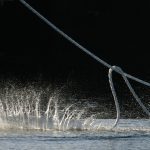 Close-up of water splashing as a mooring line is pulled taught by unseen crew on a large ship at port.