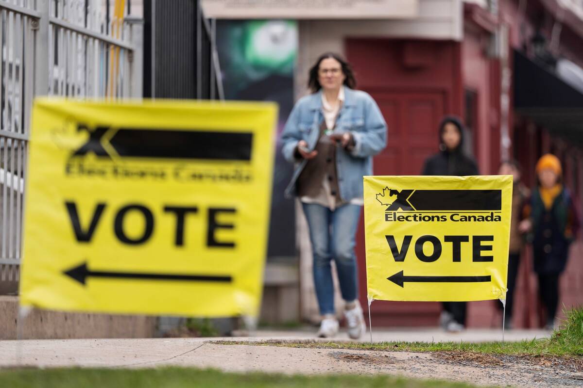 Yellow Elections Canada "Vote" signs are stuck in the grass while people walk toward them in the background.