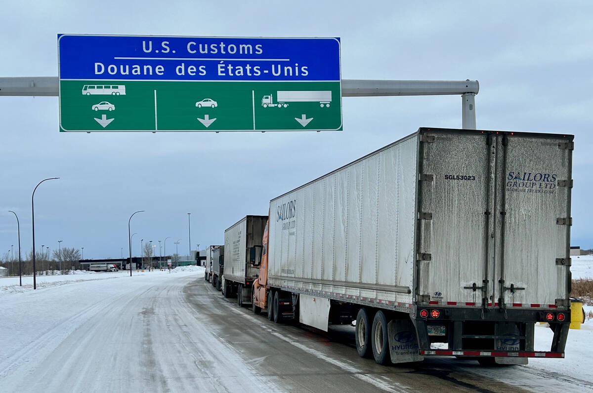 Trucks are lined up on a highway under as sign that reads, "U.S. Customs" as they wait to cross the border.