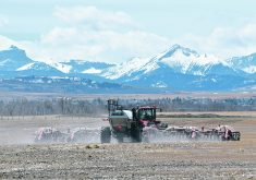 An air seeder at work on a field in Alberta with snow-capped mountains in the background.