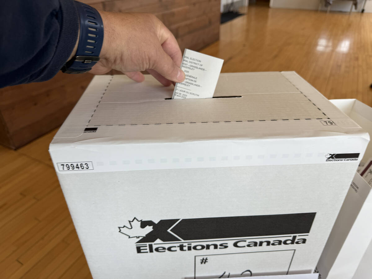 A man's hand deposits a ballot into a cardboard "Elections Canada" ballot box during voting in the 2025 federal election.