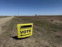 A yellow Elections Canada "Vote" sign is stuck in the ground alongside a grid road in rural Saskatchewan.