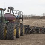 A farmer is working on top of his air seeder in the middle of a field.