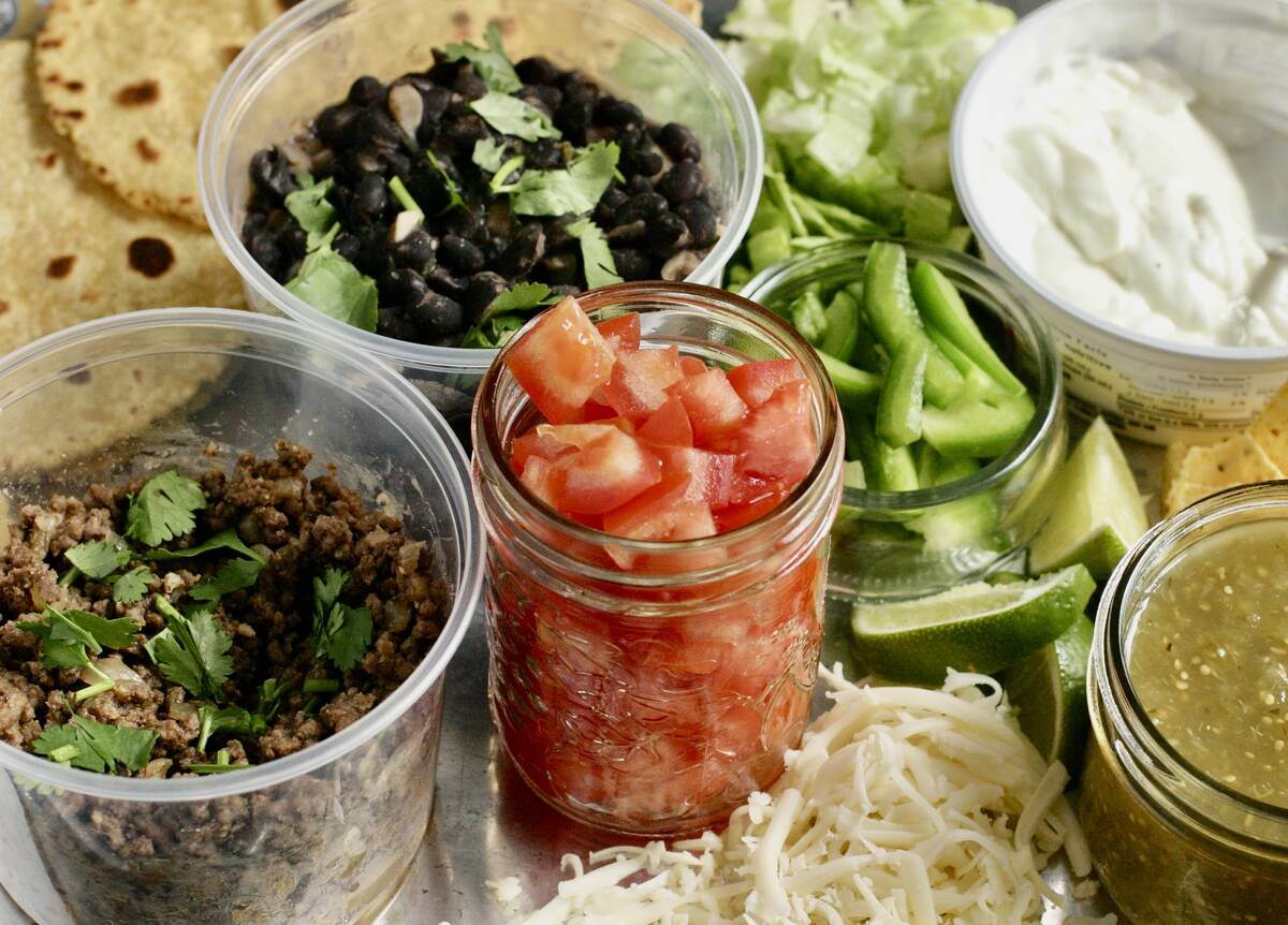 Taco ingredients like diced tomatoes, ground beef and peppers sit in containers on a table awaiting taco construction.