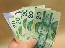 A man's hand holds a number of Canadian currency bills - five 20s and a ten.