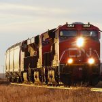 A CN locomotive pulls a grain train toward the photographer at sunset.