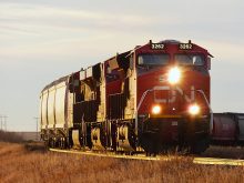 A CN locomotive pulls a grain train toward the photographer at sunset.