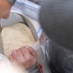 Overhead view of someone looking into a bag of flour, holding the bag open with their hands.