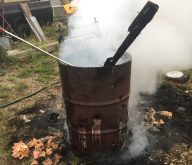A "burn barrel" in a farmyard is shown smoking and with a piece of unburned wood sticking out. The ground around it is charred.