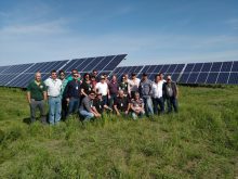 A group of people pose for a photo in front of a large solar panel array in a field.