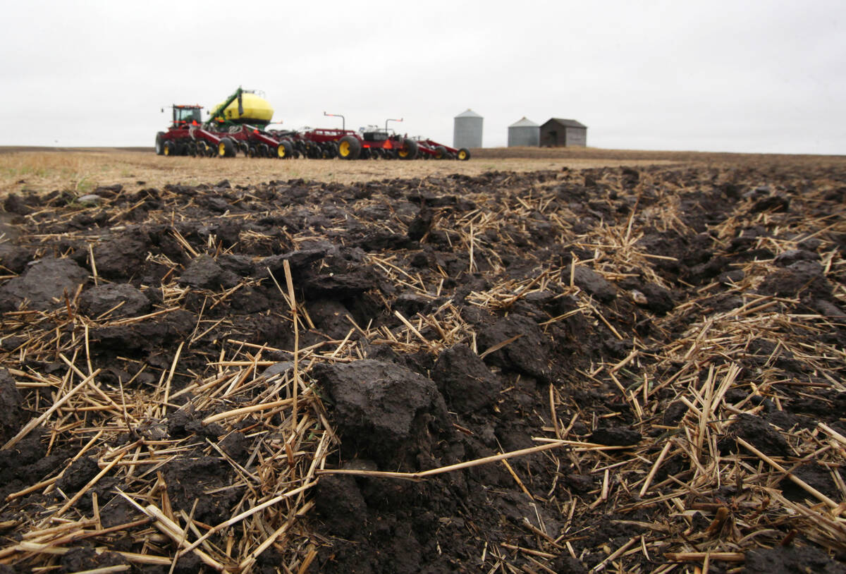 A close-up of the disturbed soil in a field with an air seeder rig in the background.