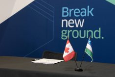 Small flags of both Canada and Uzbekistan sit on a desk with a backdrop that reads "Break New Ground" in the background.