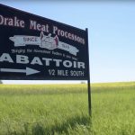 A "Drake Meat Processors" roadside sign photographed in summertime against a blue sky background.